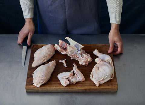 Raw cuts from a whole Yorkshire chicken presented on a wooden board.